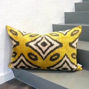 May include: A yellow and brown patterned throw pillow with a diamond design. The pillow is sitting on a gray step.