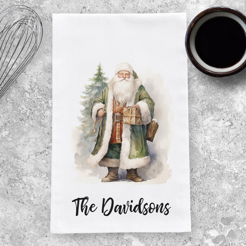 May include: A white kitchen towel with a watercolor illustration of Santa Claus holding a gift and standing next to a Christmas tree. The text "The Davidsons" is printed at the bottom of the towel.