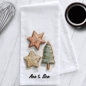 White cotton flour sack tea towel featuring watercolor art of decorated Christmas cookies – star, snowflake, and Christmas tree