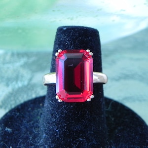 May include: A silver ring with a large, emerald-cut, red gemstone.
