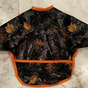 May include: Camouflage baby bib with an orange trim. The bib has a pocket in the front.