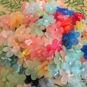 May include: A collection of colorful, sheer fabric flowers. The flowers are in various shades of pink, blue, yellow, and green. They are arranged in a random pattern and appear to be handmade.
