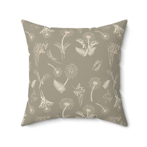 A square throw pillow with a repeating pattern of dandelions and ferns in a light brown color.