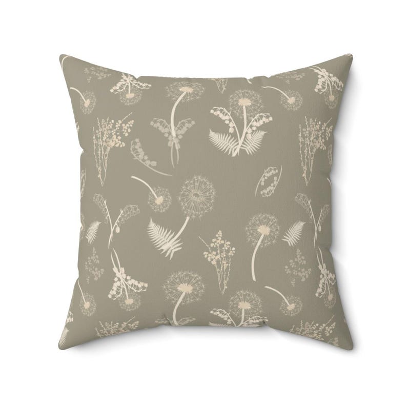 A square throw pillow with a repeating pattern of dandelions and ferns in a light brown color.