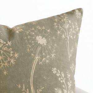 A close-up image of a decorative pillow with a floral pattern in shades of green and beige.