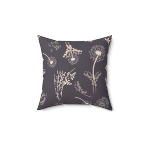 A square throw pillow with a repeating pattern of dandelions and other flowers in shades of gray and white.
