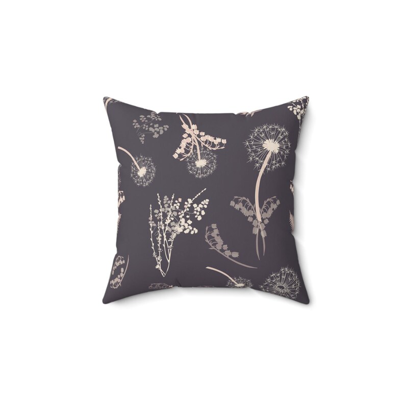 A square throw pillow with a repeating pattern of dandelions and other flowers in shades of gray and white.