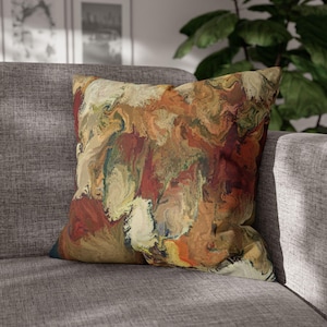 May include: Square throw pillow with an abstract design in shades of brown, red, beige, and green. The pillow has a soft, textured appearance and is placed on a gray sofa. The design resembles a watercolor painting or a marbled effect.