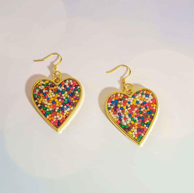 May include: A pair of gold heart-shaped earrings with colorful sprinkles embedded inside the resin.