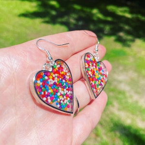May include: A pair of silver heart-shaped earrings with colorful sprinkles embedded in clear resin.