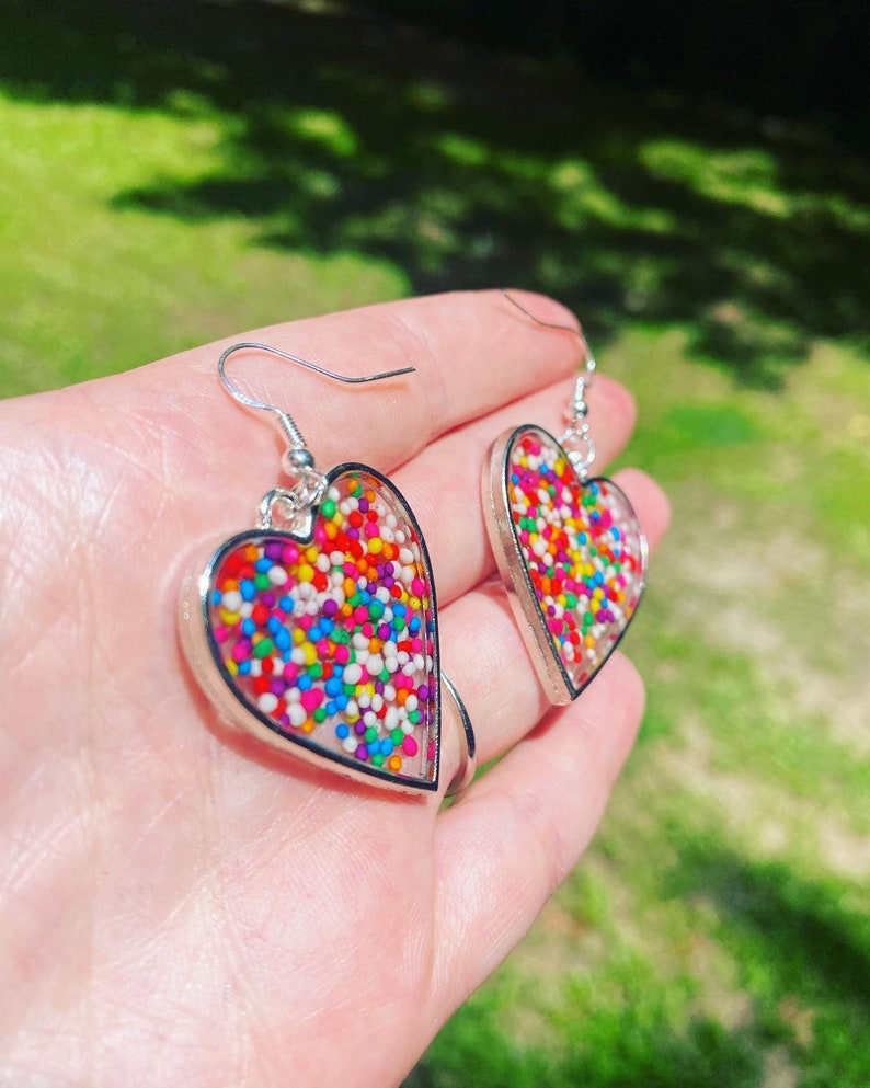 May include: A pair of silver heart-shaped earrings with colorful sprinkles embedded in clear resin.
