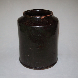 May include: A dark brown ceramic jar with a glazed finish. The jar has a rounded shape and a wide mouth.