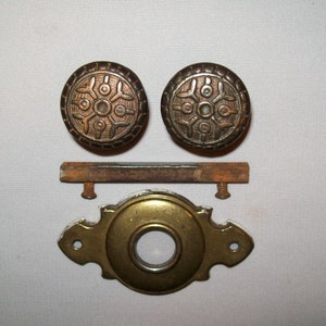 Puede incluir: Conjunto de herrajes para puertas de latón antiguo con dos pomos redondos con un diseño decorativo de copo de nieve, una placa rectangular de escudo y dos tornillos.