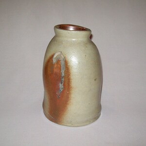 May include: A small, off-white ceramic pitcher with a brown glaze on one side. The pitcher has a chipped handle and a slightly angled opening.