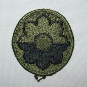 May include: A green and black embroidered patch with a stylized flower design. The flower has a central circle and eight petals.