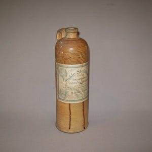 以下が含まれることがあります： 「Double Stein Style Genuine Imported Aechtler Wahl-Whiskey Imported and Bottled by F.M. Boehmer & Steinhauser The Detroit, Michigan Co.」とラベルが貼られた茶色の陶器製のボトル