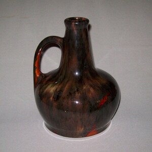 May include: A brown ceramic vase with a mottled glaze in shades of black, brown, and orange. The vase has a rounded body and a narrow neck with a single handle.