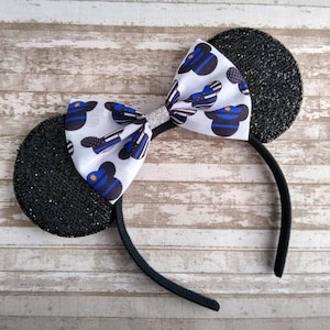 May include: Black glitter mouse ears headband with a white bow featuring a blue and white thin blue line pattern. The bow has a silver glitter center.