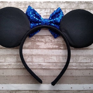May include: Black headband with large black fabric ears and a blue sequin bow.