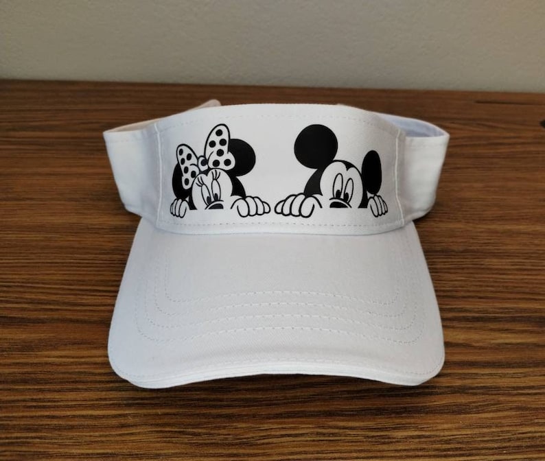 May include: White visor with a black and white image of Mickey Mouse and Minnie Mouse peeking over the top.