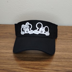 May include: Black visor with a white graphic of Mickey Mouse and Minnie Mouse peeking over the top.