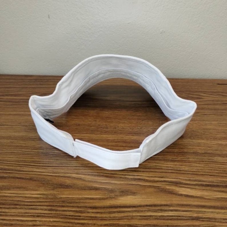May include: White visor with an adjustable strap in the back. The visor is made of a soft, flexible material.