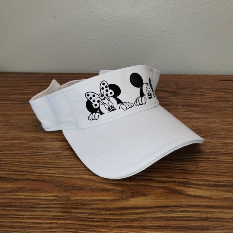 May include: White visor with a black and white image of Mickey Mouse and Minnie Mouse peeking over the top.
