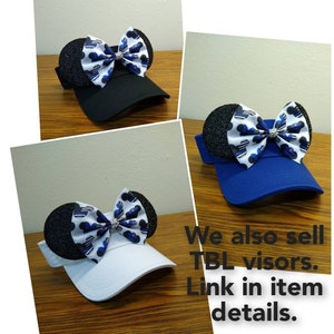 May include: Three different colored visors with a black and blue bow with a rhinestone in the center. The bow is shaped like Mickey Mouse ears. The text "We also sell TBL visors. Link in item details." is at the bottom of the image.