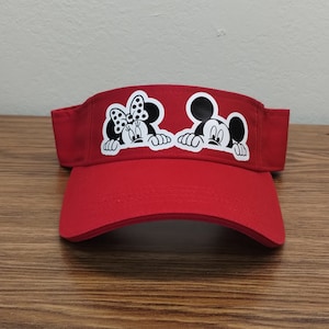 May include: Red visor with a black and white image of Mickey Mouse and Minnie Mouse peeking out from behind the brim.