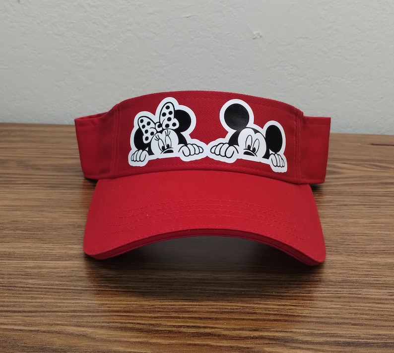 May include: Red visor with a black and white image of Mickey Mouse and Minnie Mouse peeking out from behind the brim.