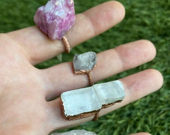 Puede incluir: Cuatro anillos con diferentes piedras de cristal envueltas en alambre de cobre. Las piedras son rosadas, blancas y transparentes.