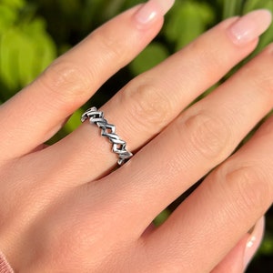 May include: A silver ring with a chain-like design. The ring is on a person's finger.