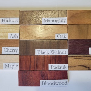 May include: A close-up of 12 wood samples, each labeled with its wood type. The wood types are Hickory, Mahogany, Canary, Ash, Oak, Teak, Cherry, Black Walnut, Purpleheart, Maple, Padauk, Zebra, and Bloodwood.