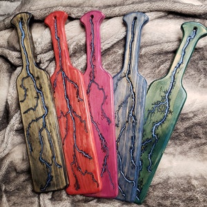 May include: Five wooden paddles with a lightning bolt design. The paddles are stained in different colors: brown, red, pink, blue, and green.