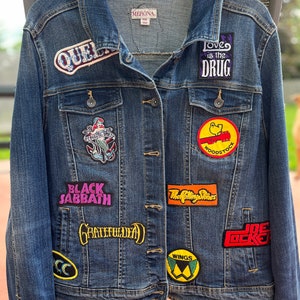 May include: A blue denim jacket with various band patches, including "Black Sabbath", "Grateful Dead", "The Rolling Stones", "Wings", "Joe Cocker", "Woodstock", "Love is the Drug", and "Queen".
