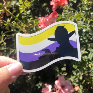 May include: A sticker with a yellow, white, and purple striped flag design. A silhouette of a person with a hat and elf ears is in the center of the flag.