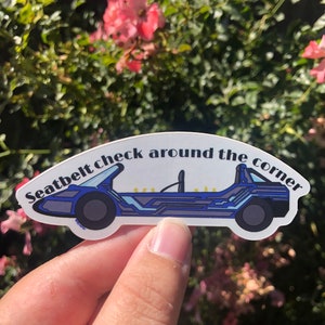 May include: A blue and gray car sticker with the text "Seatbelt check around the corner".