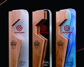 Puede incluir: Tres placas de premio con marco de madera e inserto de acrílico transparente. Las placas presentan un logotipo "J" rojo con el texto "Custom Engraved" y "Tagline Here". El texto "Award of Excellence in Performance 2022" también está incluido en cada placa. Los insertos de acrílico son blancos, negros y azules.