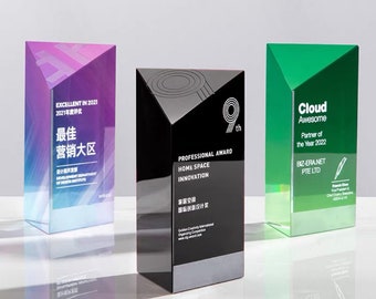 Puede incluir: Tres trofeos de cristal con bases de diferentes colores. El trofeo de la izquierda tiene una base degradada en morado y azul con el texto "EXCELLENT IN 2021 2021年度评优 最佳营销大区". El trofeo del centro tiene una base negra con el texto "PROFESSIONAL AWARD HOME SPACE INNOVATION 家居空间国际创新设计奖 9th". El trofeo de la derecha tiene una base verde con el texto "Cloud Awesome Partner of the Year 2022 BIZ-ERA.NET PTE LTD".
