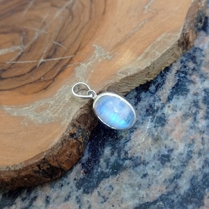 May include: A silver pendant with a blue moonstone oval cabochon. The pendant is on a wooden surface.
