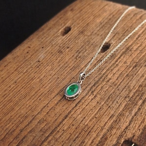 May include: A silver chain necklace with a green oval emerald pendant.