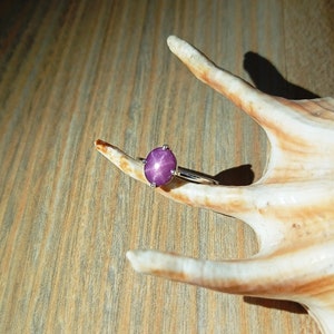 Puede incluir: Un anillo de plata con una piedra preciosa de rubí estrella redonda y púrpura.