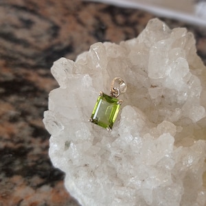 Può includere: Un ciondolo con una pietra preziosa verde con una montatura in argento. Il ciondolo è su uno sfondo bianco.