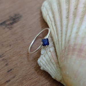Könnte beinhalten: Ein silberner Ring mit einem quadratischen, dunkelblauen Edelstein, der in einer Krappenfassung sitzt.
