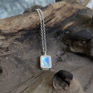 May include: A silver chain necklace with a square pendant featuring a blue iridescent gemstone.