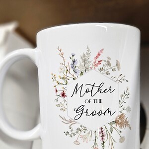 May include: White ceramic mug with a floral design and the text "Mother of the Groom".