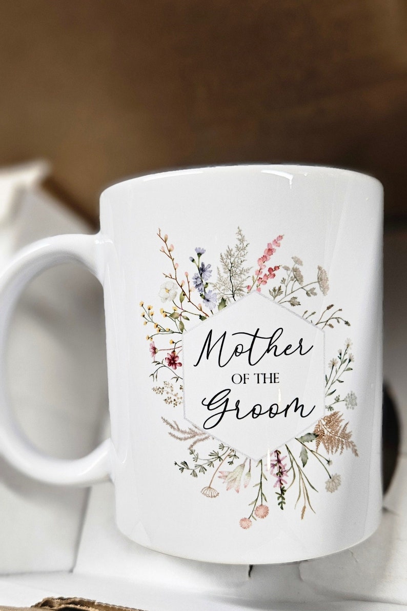 May include: White ceramic mug with a floral design and the text "Mother of the Groom".