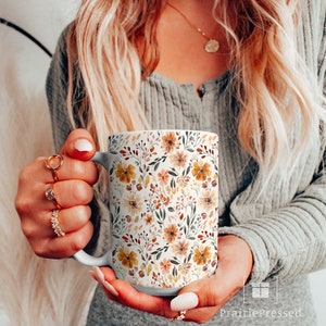 May include: White ceramic mug with a floral pattern in shades of orange, yellow, and brown. The flowers are watercolor-style and have a vintage feel.