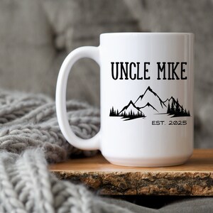 May include: White ceramic mug with a black design of mountains and the text "Uncle Mike Est. 2025".