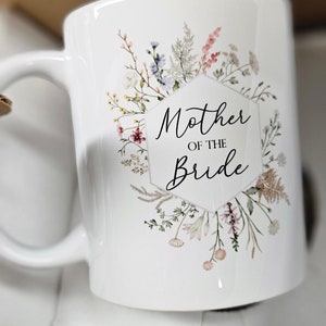May include: White ceramic mug with a floral design and the text "Mother of the Bride" in black lettering.